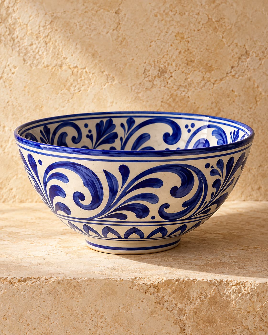 Grand bol en céramique blanche peint de volutes bleu cobalt, posé sur une pierre calcaire